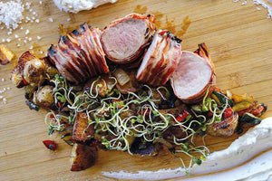 Pork loin roast wrapped in bacon with potatoes, peppers and vegetables 