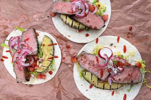 Tender brined steak tacos on a colorful bed of lettuce with grilled avocados and pickled red onions 